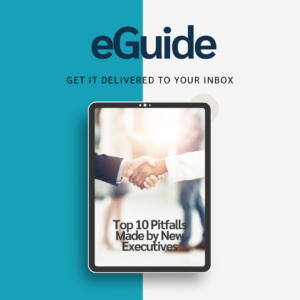 The image is a promotional graphic for an eGuide download about the Top 10 Pitfalls Made by new Executives. The background is split into two vertical sections: the left is blue and the right half is white. At the top of the image, the word "eGuide" is prominently displayed in bold, dark blue text, with the phrase "Get it delivered to your inbox" in smaller, black text beneath it. In the center of the image, there is a graphic of a tablet. The tablet screen displays the title of the eGuide, which reads: "Top 10 Pitfalls Made by New Executives" The text on the screen is black, st against a multi-color background with people shaking hands, referencing the concept of an office environment.