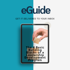 The image is a promotional graphic for an eGuide download about The 4 Basic Building Blocks of a Leadership Development Program. The background is split into two vertical sections: the left is blue and the right half is white. At the top of the image, the word "eGuide" is prominently displayed in bold, dark blue text, with the phrase "Get it delivered to your inbox" in smaller, black text beneath it. In the center of the image, there is a graphic of a tablet. The tablet screen displays the title of the eGuide, which reads: "The 4 Basic Building Blocks of a Leadership Development Program" The text on the screen is black, set against a multi-color background with a hand building something with blocks, referencing the concept of the 4 building blocks.